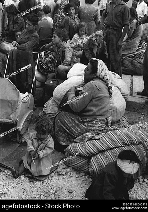 A bandaged, injured child plays in the rubble, while mother and others wait in the hope they will be taken off the Island. August 17, 1953