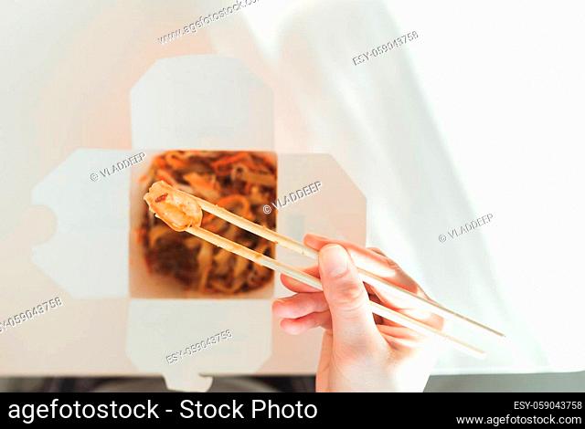 Wok noodles in takeaway box. Woman eating with chopsticks, close up view on female hands. Chinese traditional food with vegetables and seafood
