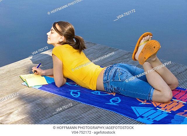 Teenaged girl lying on a footbridge and writing in her diary looking thoughtful