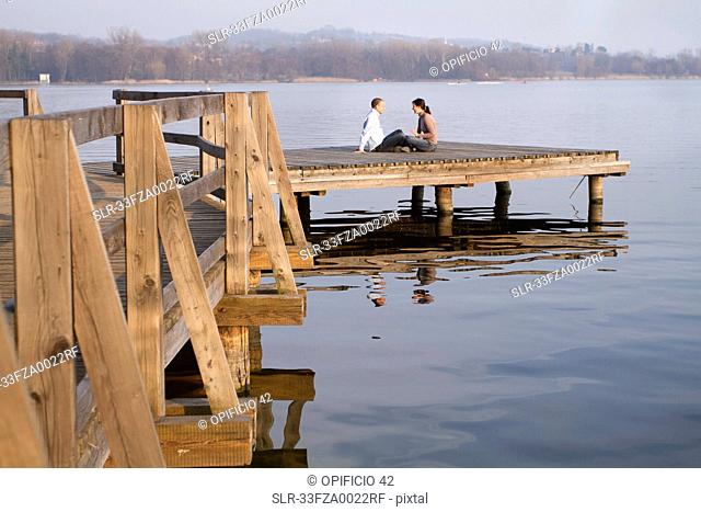 Couple talking on jetty overlooking lake