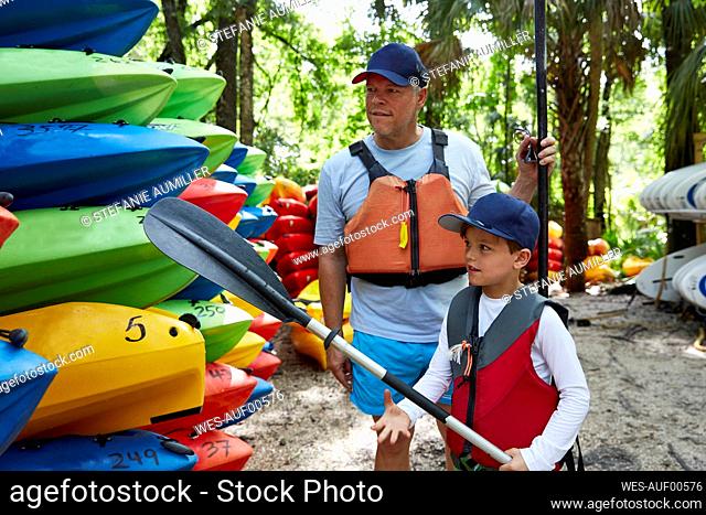 Son with oar looking at canoe while standing by father
