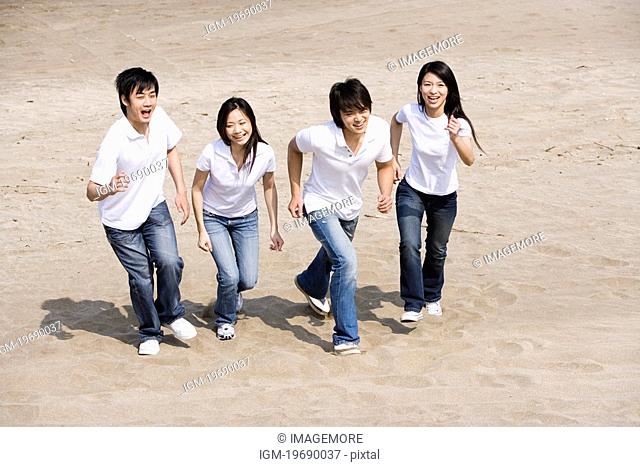 Four young adults running on beach