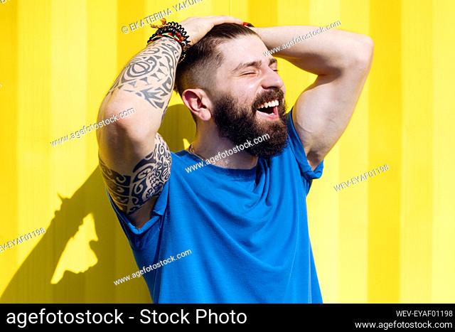 Laughing young man with tattoo standing in front of yellow wall