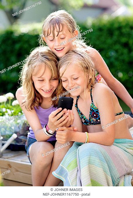 Three girls sitting in garden and texting on mobile phone