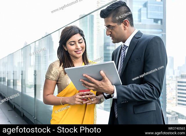 Two Indian colleagues analyzing information while using a tablet on the top of a modern building