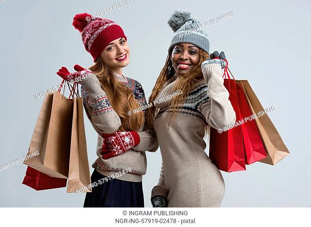 Shopping, sale, gifts, christmas, xmas concept - two smiling women in knitted dress with shopping bags