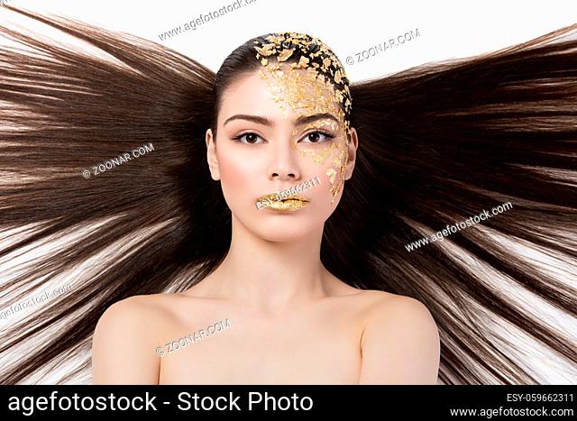 Closeup portrait of beautiful young woman with golden foil on face and lips. Creative makeup. Long hair. Isolated over white background