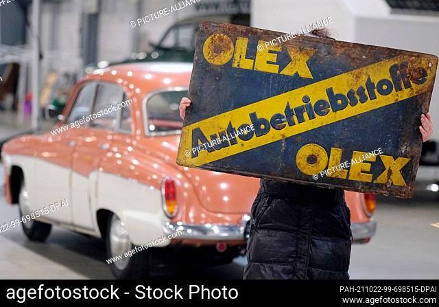 22 October 2021, Saxony-Anhalt, Halle: A trader for old automobile parts holds an old advertising sign in her hands. The piece will be on offer at the...