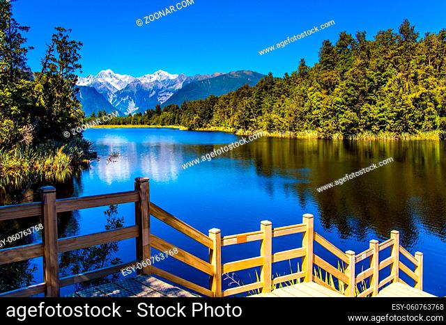 Magnificent snow-capped mountains and forests surround the Lake Matheson. Mirror glacial lake Lake Matheson is surrounded by mountains Steps go down to the...