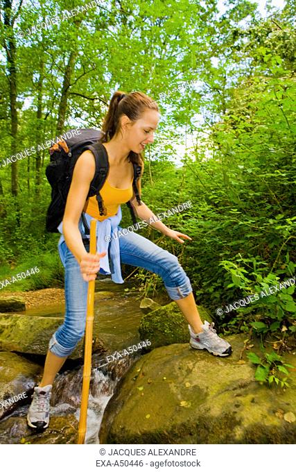 Young woman hiking through the woods and trying to cross a stream
