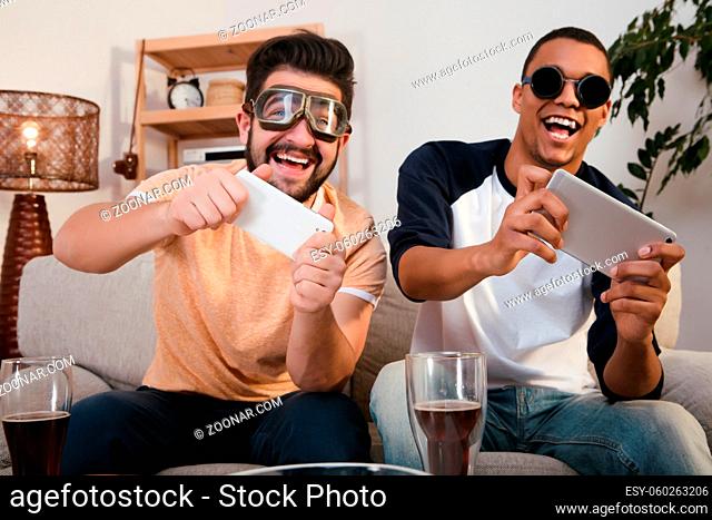 Picture of happy friends playing computer games and looking at TV screen. Handsome man with special glasses on using mobile or smart phones
