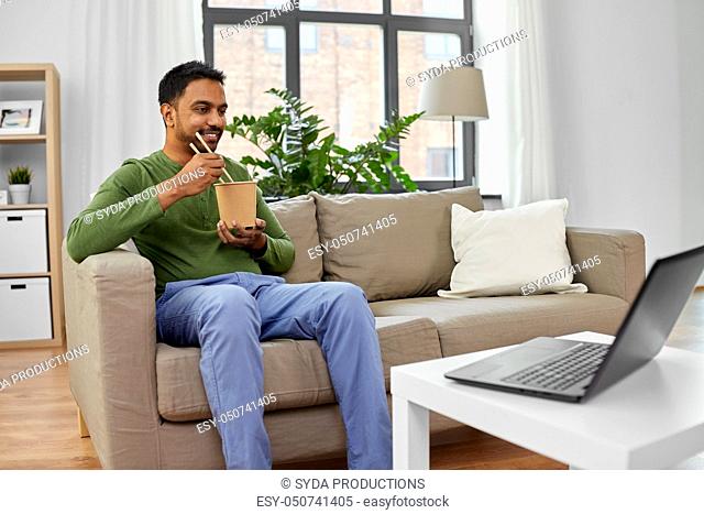 indian man with laptop eating takeout food at home