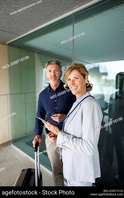 Businesswoman holding mobile phone standing with businessman in front of glass wall