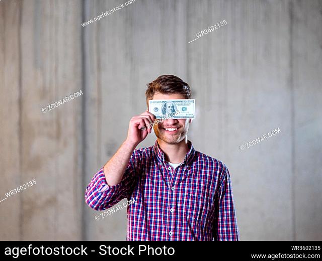 business, people and finances concept happy young business man holding american dollars banknote over the eyes in new startup office