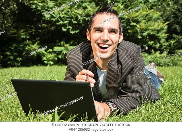 Young man working outdoors on his laptop, smiling at the camera