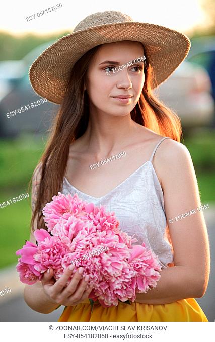 portrait of a beautiful, young, happy girl with a bouquet of peonies in the light of the setting sun in the evening