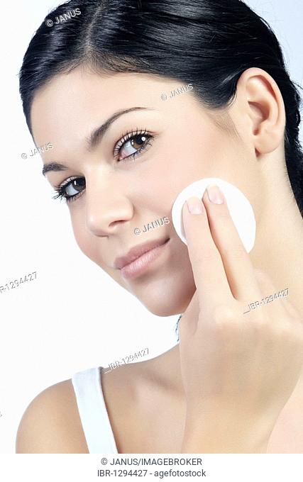 Young woman using a cotton pad for cleansing, looking directly at the viewer, beauty