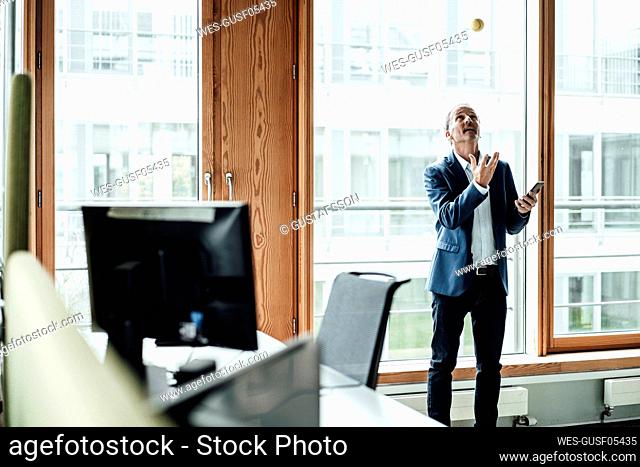 Playful businessman throwing ball against glass window in office