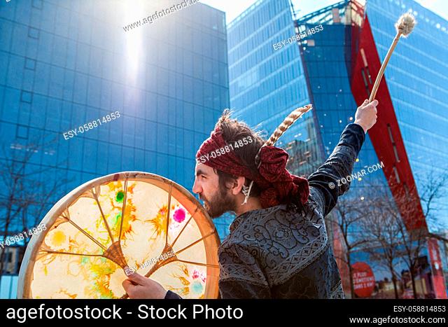 A closeup view of a spiritual guy playing a traditional drum downtown, seeks inspiration from city surroundings. Blurred skyscrapers in background
