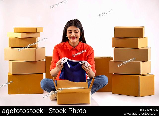 A young woman unpacking new dress sitting amidst cardboard boxes