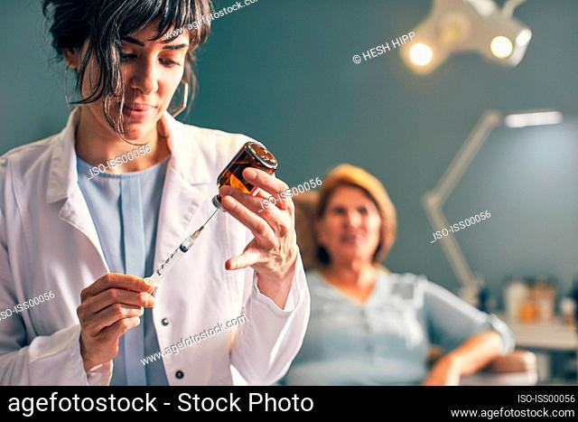 Female doctor preparing botox injection, patient in background
