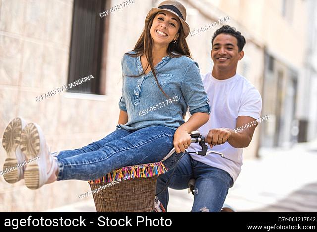 Joyful couple riding bicycle outdoors in city. Man with delighted woman sitting on handlebar while riding bicycle in city