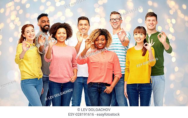 diversity, race, ethnicity and people concept - international group of happy smiling men and women showing ok hand sign over holidays lights background