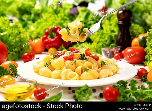 Plate of cooked italian pasta, pipe rigate on fork with tomatoes and basil leaves