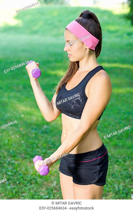 Fitness Slim Woman Training with dumbbells. Attractive Female practicing using hand weights outdoor