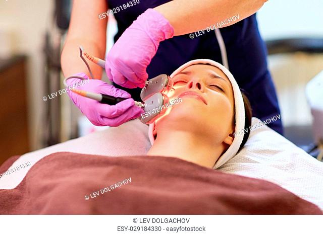 people, beauty, cosmetic treatment, cosmetology and technology concept - beautician with microdermabrasion device doing face exfoliation to young woman lying at...