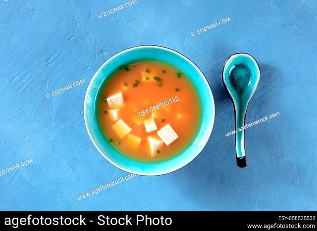Miso soup with tofu and green onions, shot from the top on a blue background