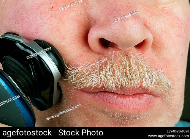 Elderly old man cuts hairs on his face  with an electric shaver. Studio macro natural colors simplistic image