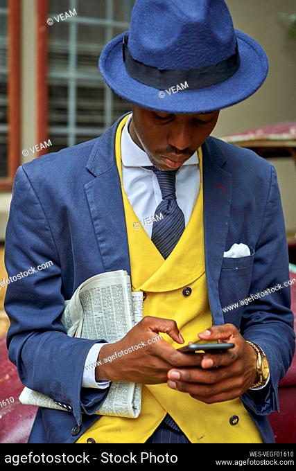 Young businessman wearing old-fashioned suit and hat checking his phone