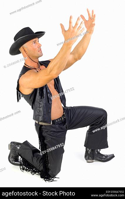 Handsome man kneeling in cowboy costume. Holding hands up in prayer. Isolated on white in studio, side view