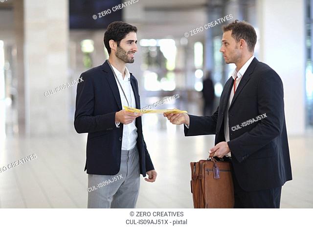 Office worker handing paperwork to businessman in conference centre