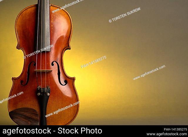 An old violin with slight scratches and damage in the bleed against a neutral, yellow background with free space for text. | usage worldwide