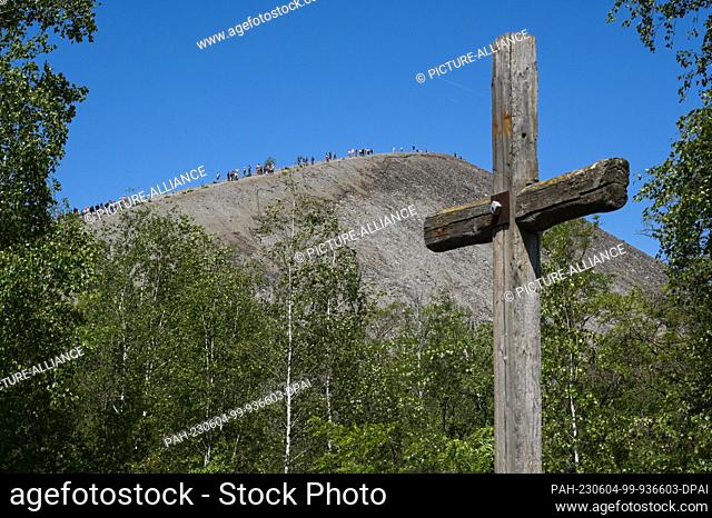 04 June 2023, Saxony-Anhalt, Volkstedt: A Jesus cross made of wooden sleepers in front of the spoil heap where visitors have made their way to the top