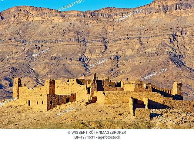 Ruined Kasbah on a hill, a former Berbers' house built of adobe, mountain range of the Djebel Kissane table mountain at the back, Draa Valley, southern Morocco
