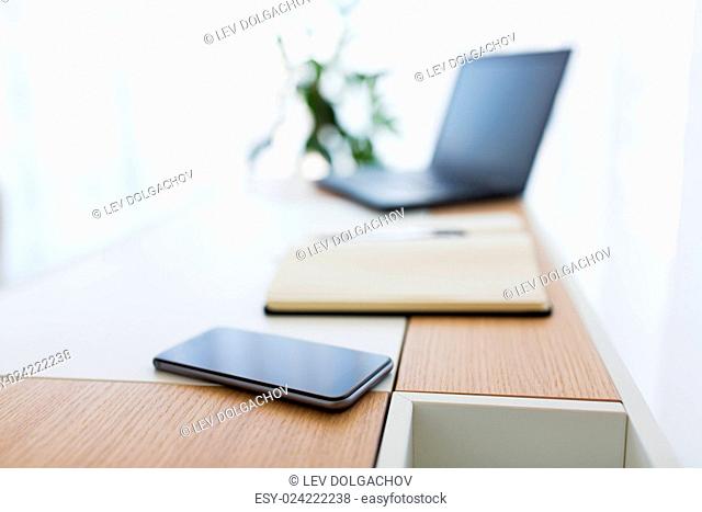 business, objects and education concept - close up of office workplace with notebook, laptop computer and smartphone on table