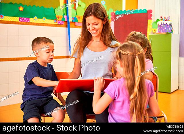 Tagesmutter oder Erzieherin beim Buch vorlesen für eine Kinder Gruppe im Kindergarten