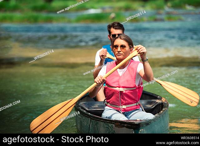 Couple friends are canoeing in a wild river surrounded by the beautiful nature