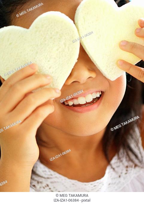 Close-up of a girl holding two heart shaped breads in front of her eyes