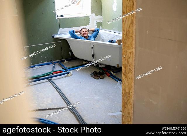 Happy man with hands behind head lying in bathtub in attic