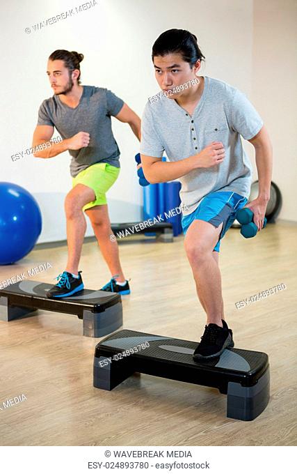 Two men doing step aerobic exercise with dumbbell on stepper