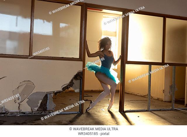 Front view of a young mixed race female ballet dancer wearing a blue tutu and pointe shoes dancing in a doorway at an abandoned warehouse building