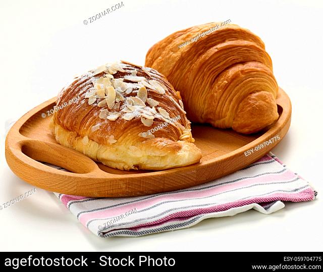 Baked crisp croissant on wooden board, white table. Breakfast