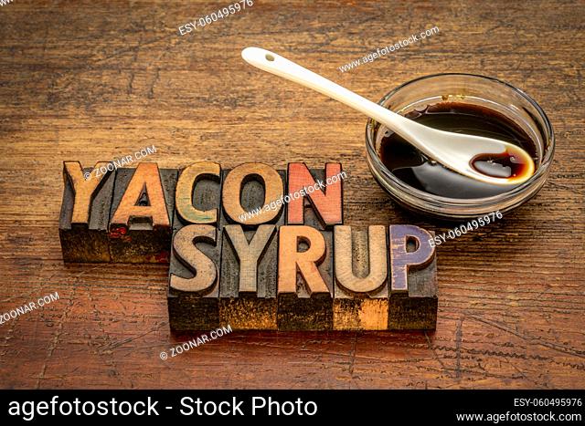a small bowl of yacon syrup against rustic weathered wood with text in vintage letterpress printing blocks, a powerful prebiotic sweetener derived from the...