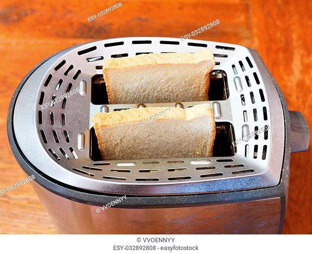 two fresh slices of bread in metal toaster on wooden table