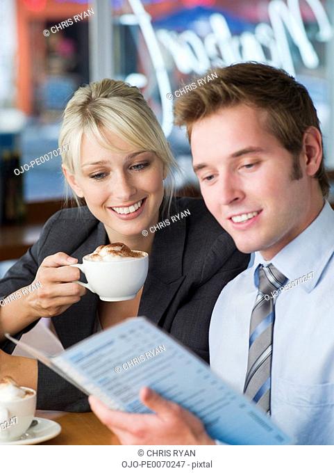 Businessman and businesswoman with lattes looking at cafe menu