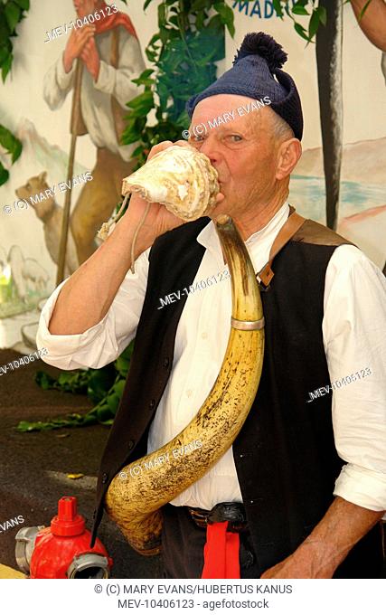 A man belonging to a Porto da Cruz folklore group, using a shell as a bugle and a cow horn as a wine container. He is taking part in street entertainment in...